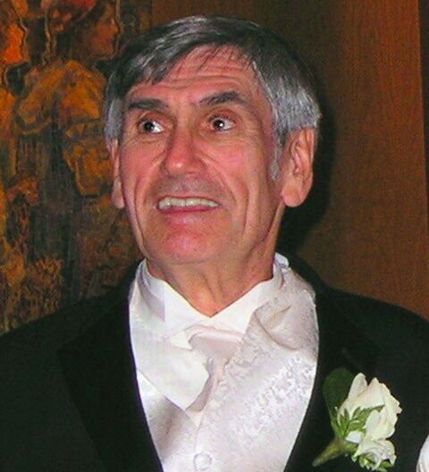 Marshall B. Rosenberg trägt einen eleganten Anzug mit einer weissen Steckblume und schaut verschmitzt nach links oben.